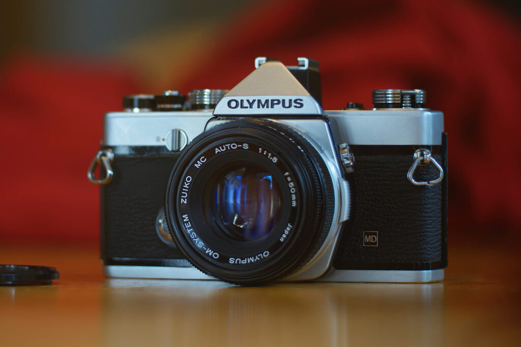 Olympus OM-1 argentique entre les mains d’un photographe de rue, lumière dorée du soir.