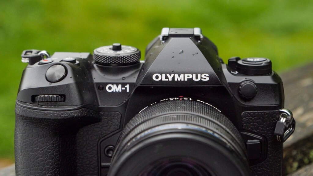 Appareil photo OM System OM-1 utilisé en nature sous la pluie, illustrant sa tropicalisation et sa robustesse pour le reportage et la photo de terrain.