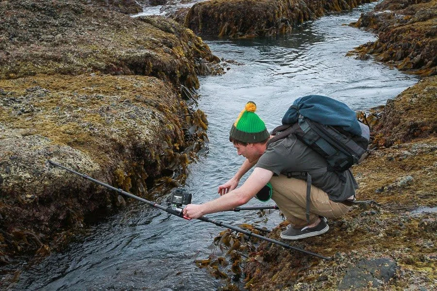 Photographe professionnel installant correctement un trépied sur un terrain irrégulier pour une photo de paysage nette.