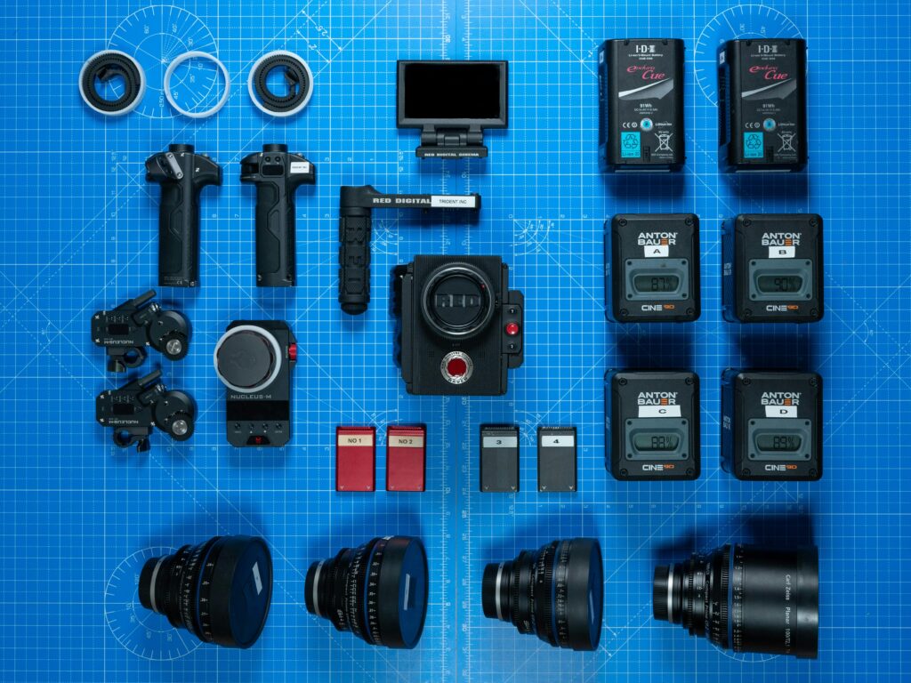 Ensemble d’accessoires vidéo comprenant micro externe, trépied, batterie et cartes SD, évoquant la préparation et le soin du matériel vidéo.